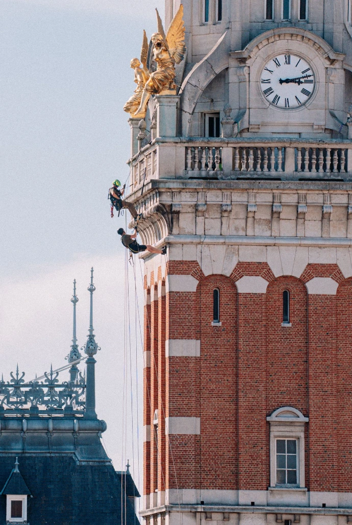 Cordiste spécialisé effectuant des travaux de restauration ou d&#39;inspection sur la façade et la tour de l&#39;horloge d&#39;un bâtiment historique en pierre.