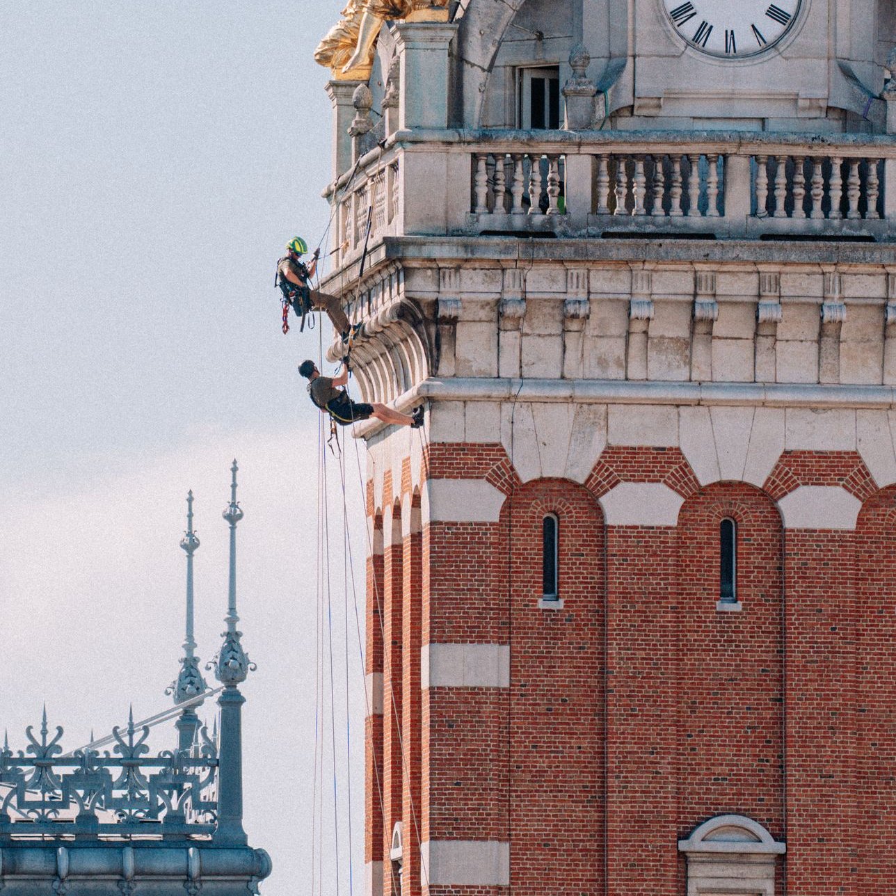 Cordiste spécialisé effectuant des travaux de restauration ou d&amp;#39;inspection sur la façade et la tour de l&amp;#39;horloge d&amp;#39;un bâtiment historique en pierre.