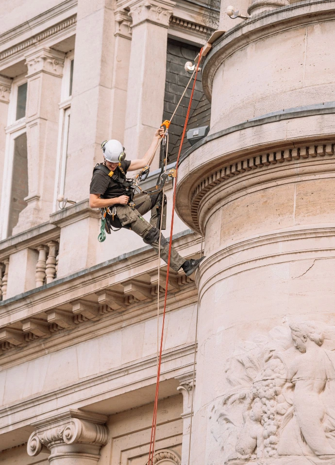 Technicien cordiste équipé effectuant une intervention de sécurisation et de maintenance sur la façade d&#39;un immeuble en milieu urbain