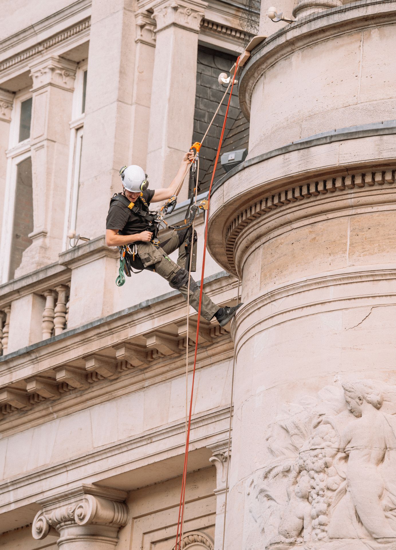 Technicien cordiste équipé effectuant une intervention de sécurisation et de maintenance sur la façade d&amp;#39;un immeuble en milieu urbain