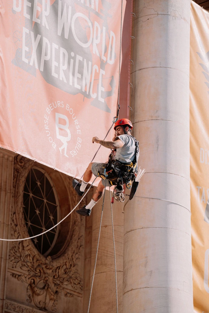 Installation d&amp;#39;une bâche publicitaire grand format sur un bâtiment historique à Bruxelles par un cordiste spécialisé en événementiel.